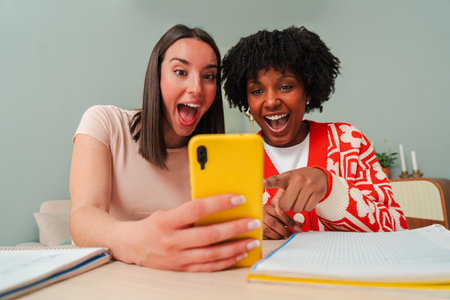 Excited women sharing joyful moments while watching a captivating video on a bright yellow smartphone together, showcasing their genuine reactions andの写真素材