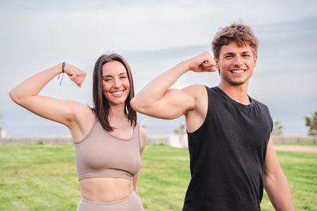 Energetic couple demonstrating strength and fitness with powerful arm flexing poses outdoors