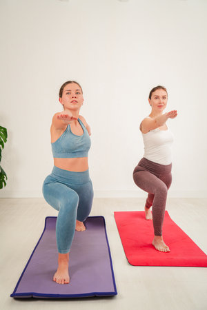 Two dedicated women performing yoga poses together in a serene indoor space focused on strength, balance, and flexibility while enhancing theirの写真素材