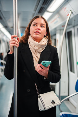 Young woman standing in a subway train while using her smartphone to browse the internet and interact with mobile applications during her dailyの写真素材