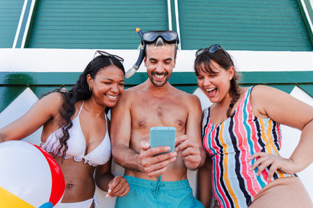 Friends enjoying a sunny beach day together while laughing and sharing fun moments with a phoneの写真素材