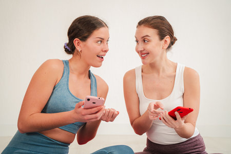 Two enthusiastic women joyfully sharing their excitement while using smartphones to engage with each other and explore new apps, showcasing the joy ofの写真素材