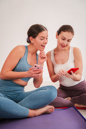 Two enthusiastic women engaging with their smartphones while sharing ideas and experiences in a fun and interactive manner during a relaxed moment ofの写真素材