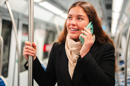 Cheerful woman engaging in a lively phone conversation while standing in a subway train, showcasing her joyful expression and connection through herの写真素材