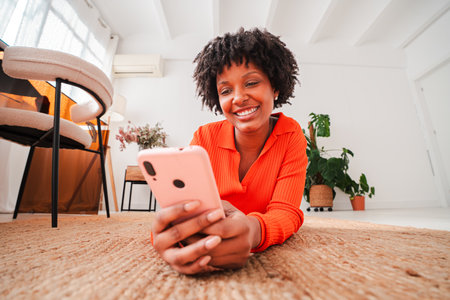 Happy woman lying on the floor while using her mobile phone to connect and engage with friends through social media or messaging applications in aの写真素材