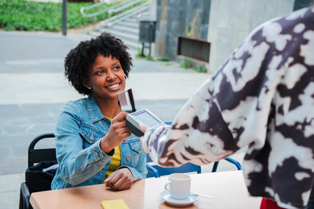 Woman happily paying with credit card while seated at a table in a lively outdoor cafe atmosphereの写真素材