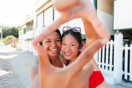 Two joyful girls enjoying a sunny day at the beach while playfully framing a fun moment togetherの写真素材