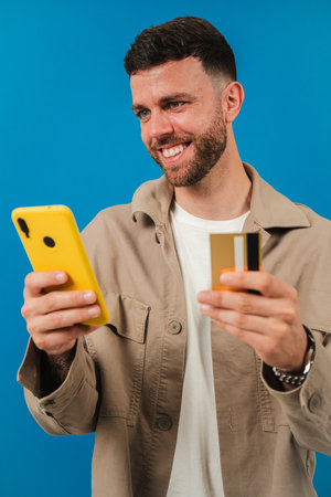 Young man enjoys shopping online while using a smartphone and holding a credit card in his handの写真素材
