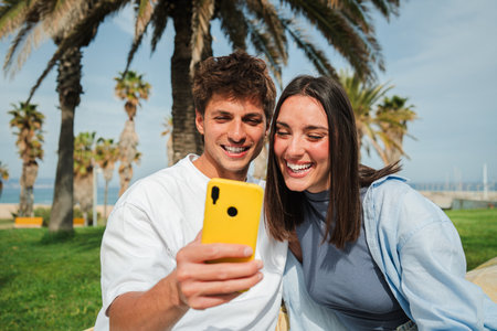 Joyful couple sharing a delightful moment while browsing their smartphone in a beautiful outdoor settingの写真素材