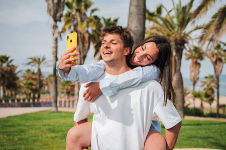 Happy couple enjoying a playful moment while taking a cheerful selfie on a sunny day outdoorsの写真素材