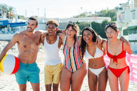 Joyful friends enjoying a sunny day at the beach with laughter, games, and a colorful beach ballの写真素材