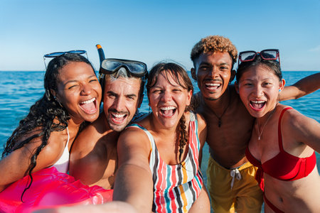 Joyful group of friends enjoying a sunny day at the beach while taking a fun selfie in the seaの写真素材