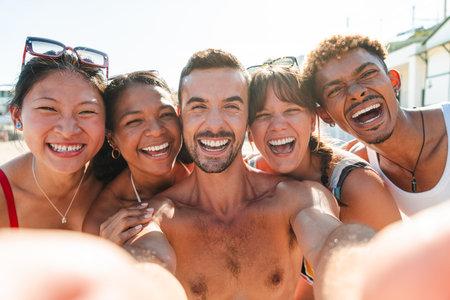 Joyful friends enjoying a sunny beach day together while taking a cheerful selfie at the shoreの写真素材