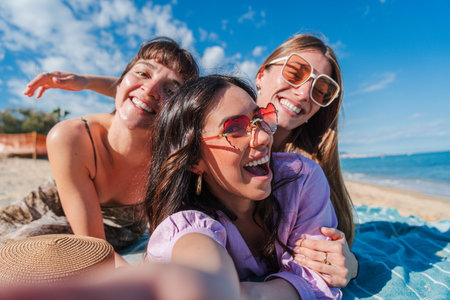 Three joyful friends capturing a lively selfie on a sunny beach during a fun-filled summer dayの写真素材