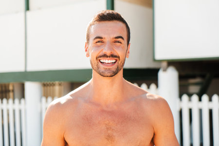 Joyful young man smiling brightly while enjoying a sunny day at the beach near the coastline shoreの写真素材