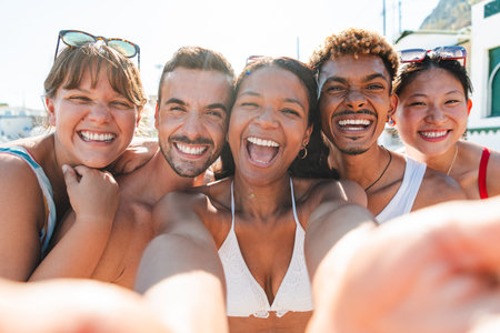 Joyful friends enjoying a sunny beach day together while taking a fun selfie with laughter and smilesの写真素材