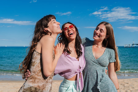 Three joyful young women laughing and enjoying their time together at a sunny beach by the oceanの写真素材