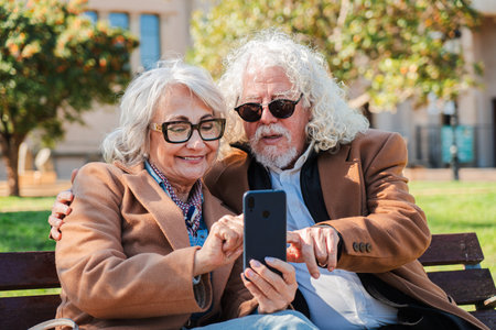 Joyful seniors engaged in cheerful conversation while exploring a smartphone together, sharing laughter and delight during their leisurely time in theの写真素材