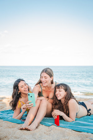 Three joyful friends enjoying their time together, sharing a fun moment while using a smartphoneの写真素材