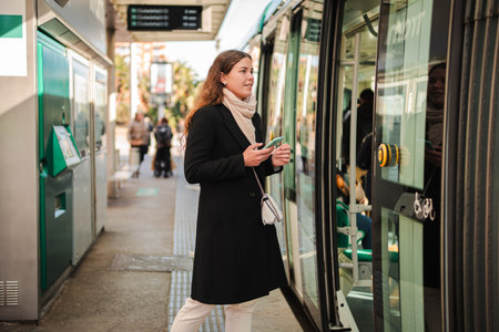 Woman standing at the subway station entrance looking at her phone while waiting for the transport to arrive with anticipation and eagerness toの写真素材