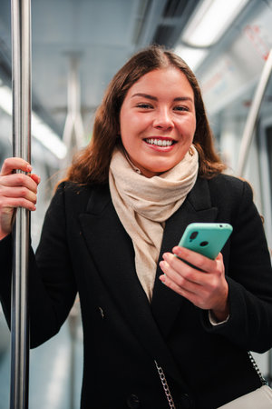 Cheerful young woman happily using her smartphone while enjoying a ride on the subway, staying connected and engaged with her mobile device during herの写真素材