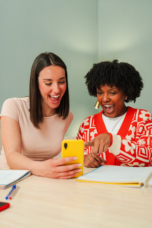 Two enthusiastic women joyfully sharing a moment while watching something entertaining on a smartphone device, highlighting their friendship andの写真素材