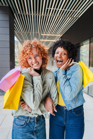 Two cheerful girls enjoying a fun shopping day with colorful bags and bright smiles while posingの写真素材