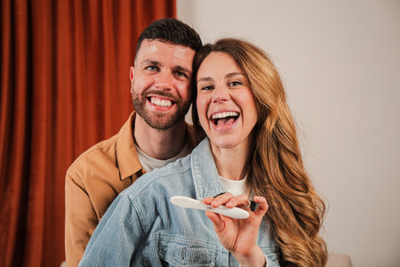 Joyful couple celebrating exciting pregnancy news with a positive test in their cozy living roomの写真素材