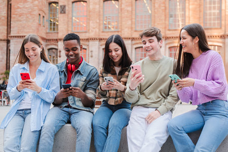 Group of cheerful young friends enjoying their smartphones while sharing laughter and fun togetherの写真素材