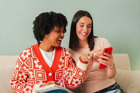 Two cheerful women joyfully engaging with a cellphone while sharing a delightful moment of laughter and conversation, showcasing friendship andの写真素材