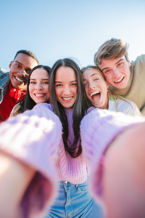 Vertical selfie portrait of a group of young multiracial teenagers having fun on a friendly meeting....