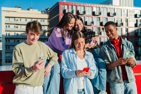 Five diverse young friends joyfully engaging with their smartphones while sharing experiences...