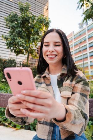 Vertical Young hispanic woman texting and sending messages with a mobilephone. Latina girl having...