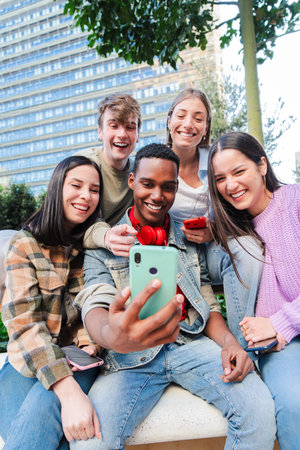 Vertical. Multiracial group of friends enjoying and smiling using a cellphone app. Diverse teenagers...