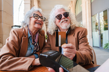 Cheerful elderly couple happily making a payment with a credit card at a stylish cafe, showcasing their joy and connection during a delightful outingの写真素材