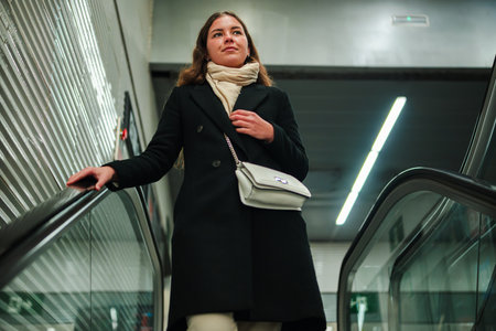 Young woman confidently riding the escalator while looking ahead, showcasing determination and focus...