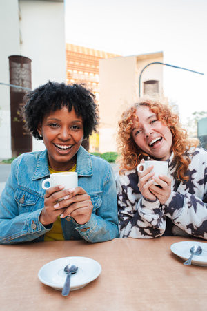 Two joyful women enjoying a warm beverage together while sharing laughter and delightful momentsの写真素材