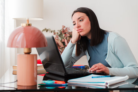 Frustrated young woman struggling with laptop while typing and looking stressed at home during...