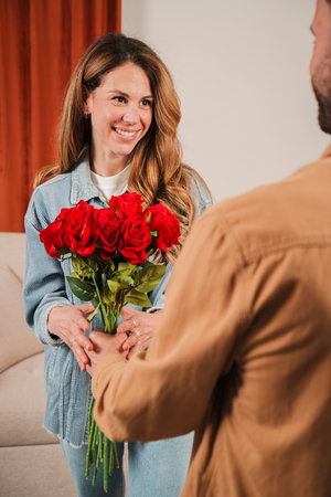 Joyful woman receiving beautiful bouquet of red roses from her partner in a warm and inviting settingの写真素材