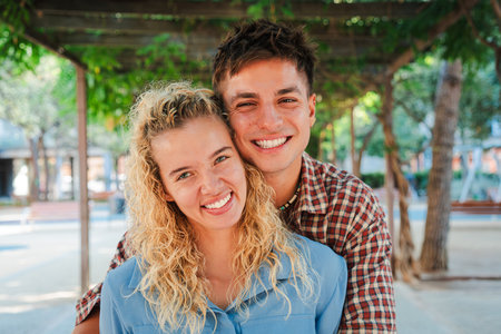 Joyful couple sharing a warm embrace while smiling brightly at the camera in a beautiful outdoor settingの写真素材