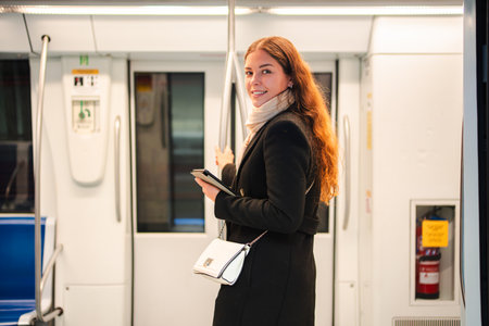 Young woman joyfully using her smartphone while standing in a public transport subway train, smiling and enjoying the convenience of modern technologyの写真素材