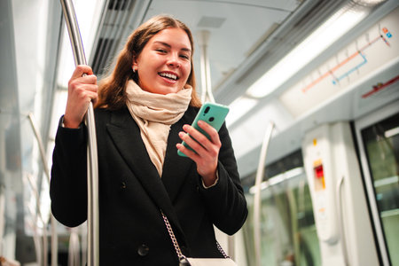Happy woman enjoying her smartphone while commuting on the subway, browsing through applications and engaging with friends during her daily travelの写真素材