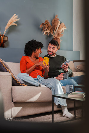 Happy couple enjoying quality time together while using their smartphones on a cozy couch at home