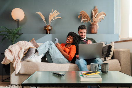 Couple engaged in online shopping on laptop and smartphone while relaxing together on couch