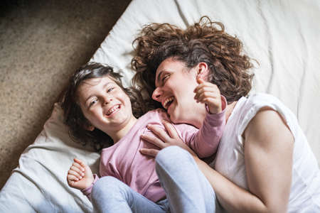 A mother tickles her daughter and laughs out loud while playing on the bedの写真素材