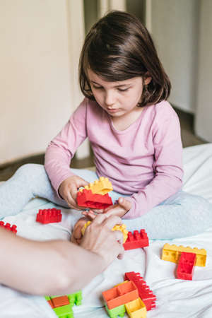 A mother and her daughter sitting down on a bed play games by joining some toy bricks togetherの写真素材