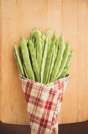 A bunch of string beans wrapped in a table cloth lay as a vegetable bouquet on a wooden backgroundの写真素材