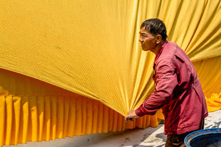 Ayutthaya, Thailand - March 8th 2013. Old thai man stretches a yellow gaudy robe of a giant laying Buddha statueのeditorial素材