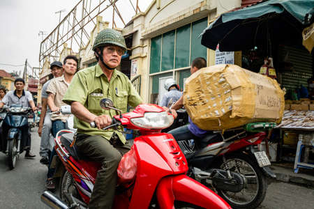 Hanoi, Vietnam - March 26th 2013. An old man in military clothes rides a red motorcycle through the busy streets of a local market. His bike helmet resembles the one of a soldier'sのeditorial素材