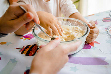 A mother stirs flour dough as her daughter kneads it with her hands. They are making homemade plasticine, the bowl sits on a colorful party tableclothの写真素材